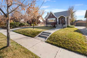 View of front of property featuring brick siding, a chimney, a front lawn, an outbuilding, and a garage