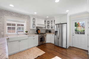 Kitchen featuring stainless steel appliances, glass insert cabinets, white cabinets, dark wood-style floors, and light stone countertops
