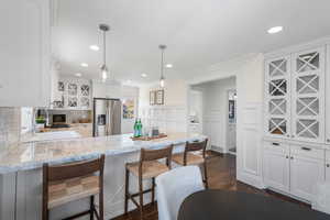 Kitchen with glass insert cabinets, stainless steel fridge with ice dispenser, a peninsula, a kitchen bar, and pendant lighting