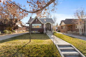 View of front of property featuring brick siding, a front yard, and a chimney