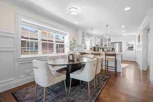 Dining room featuring a decorative wall, crown molding, dark wood-type flooring, recessed lighting, and wainscoting