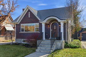 View of front facade with brick siding, a front lawn, a garage, an outbuilding, and a shingled roof