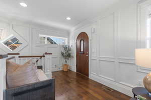 Entryway featuring a decorative wall, dark wood-style flooring, ornamental molding, and recessed lighting