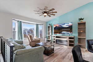 Living room with light wood finished floors, a ceiling fan, vaulted ceiling, and a glass covered fireplace