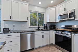 Kitchen featuring appliances with stainless steel finishes, white cabinetry, light wood-style floors, dark stone counters, and recessed lighting