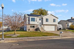 Split foyer home with concrete driveway, solar panels, a garage, and brick siding