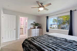 Bedroom with light colored carpet, ceiling fan, and connected bathroom