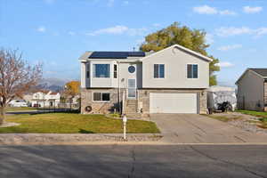 Raised ranch featuring driveway, solar panels, brick siding, and an attached garage