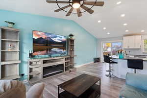 Living room featuring lofted ceiling, light wood-type flooring, recessed lighting, a ceiling fan, and a glass covered fireplace