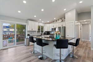 Kitchen featuring a breakfast bar area, a center island, appliances with stainless steel finishes, white cabinets, and dark stone counters