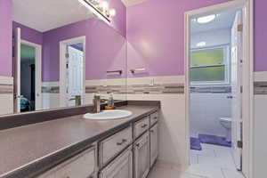 Bathroom featuring vanity, tile walls, wainscoting, light tile patterned flooring, and a textured ceiling