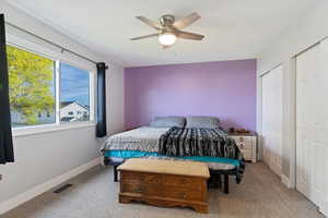 Bedroom with light colored carpet, multiple closets, and a ceiling fan