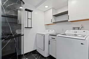 Laundry area featuring dark marble finish floors, cabinet space, and washing machine and clothes dryer