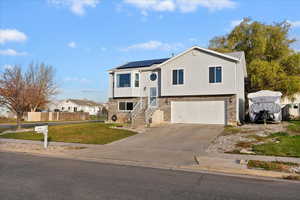 Raised ranch featuring solar panels, driveway, a garage, and brick siding
