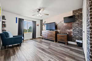 Living area with brick wall, wood finished floors, an accent wall, and a ceiling fan