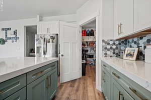 Kitchen with green cabinets, white cabinetry, stainless steel refrigerator with ice dispenser, and light wood-style floors