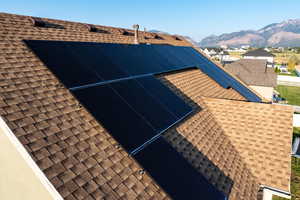 View of property exterior featuring roof with shingles, a mountain view, and roof mounted solar panels