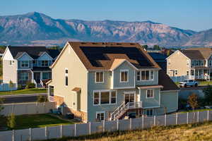 Back of house featuring a fenced backyard, roof mounted solar panels, a residential view, a mountain view, and stairway