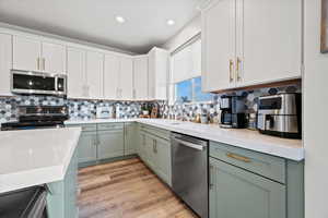 Kitchen featuring appliances with stainless steel finishes, white cabinets, light wood-style flooring, light stone counters, and recessed lighting