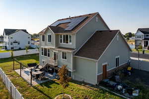 Back of house featuring a patio, a fenced backyard, solar panels, and a shingled roof