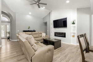 Living room with lofted ceiling, built in shelves, light wood finished floors, arched walkways, and a ceiling fan