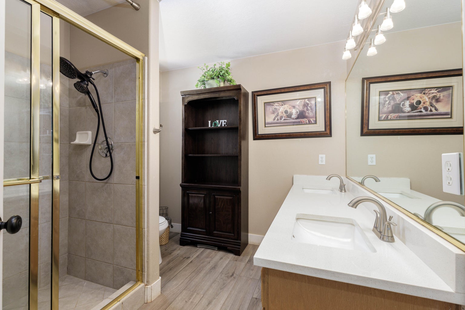 Full bathroom with double vanity, a shower stall, and light wood-type flooring