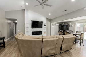 Living room with lofted ceiling, built in shelves, ceiling fan, light wood-style flooring, and a glass covered fireplace