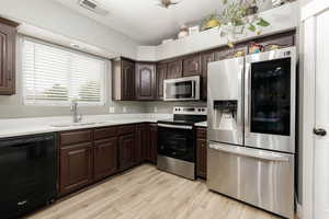 Kitchen featuring stainless steel appliances, dark brown cabinets, and light wood finished floors