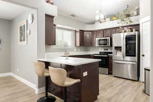 Kitchen featuring stainless steel appliances, a peninsula, a kitchen bar, dark brown cabinets, and light wood finished floors
