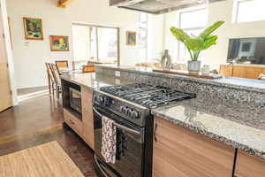 Kitchen featuring range with gas cooktop, light stone counters, finished concrete flooring, modern cabinets, and range hood