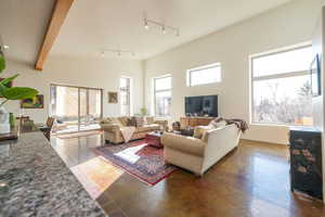 Living area with plenty of natural light, beamed ceiling, concrete floors, and a towering ceiling