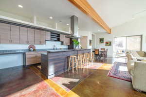 Kitchen with a kitchen breakfast bar, concrete flooring, dark stone counters, island range hood, and open floor plan