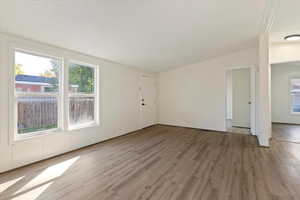 Unfurnished living room featuring a textured ceiling, light wood-style flooring, healthy amount of natural light, and lofted ceiling