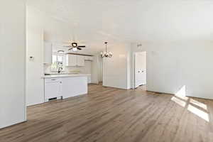 Unfurnished living room with a chandelier, light wood-style floors, a textured ceiling, and lofted ceiling