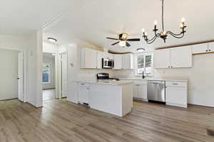 Kitchen featuring light countertops, decorative light fixtures, white cabinets, appliances with stainless steel finishes, and light wood finished floors