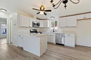 Kitchen featuring light countertops, white cabinets, stainless steel appliances, light wood-style floors, and a peninsula