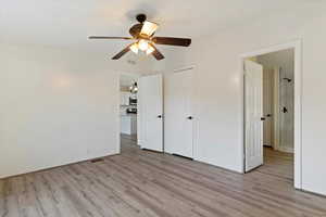 Unfurnished bedroom with light wood finished floors, ceiling fan, and ensuite bath