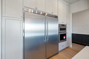 Kitchen with appliances with stainless steel finishes, white cabinetry, light wood-type flooring, light stone counters, and decorative backsplash