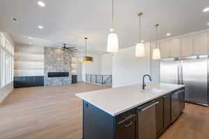 Kitchen featuring hanging light fixtures, appliances with stainless steel finishes, open floor plan, an island with sink, and light wood-style floors