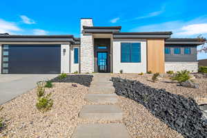 View of front facade with stone siding, concrete driveway, a chimney, stucco siding, and an attached garage