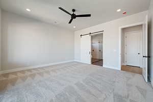 Unfurnished bedroom with a barn door, a ceiling fan, connected bathroom, carpet floors, and recessed lighting