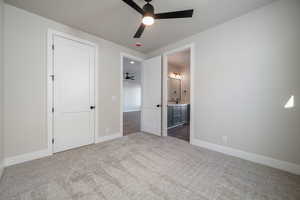 Unfurnished bedroom with dark colored carpet, ceiling fan, and ensuite bath