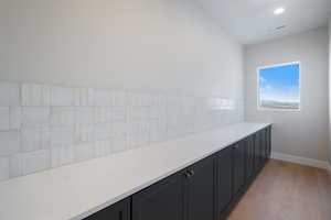 Kitchen featuring light stone counters, dark cabinetry, light wood-type flooring, decorative backsplash, and recessed lighting