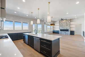 Kitchen featuring a kitchen island with sink, light wood-type flooring, light stone counters, dark cabinets, and recessed lighting