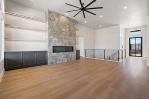 Unfurnished living room with a tiled fireplace, light wood-style flooring, recessed lighting, built in features, and a ceiling fan