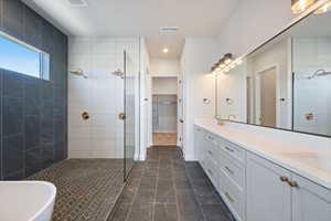 Full bathroom featuring a tile shower, double vanity, a spacious closet, a freestanding tub, and dark marble finish flooring