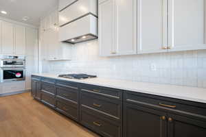 Kitchen with white cabinets, backsplash, premium range hood, light wood finished floors, and stainless steel appliances