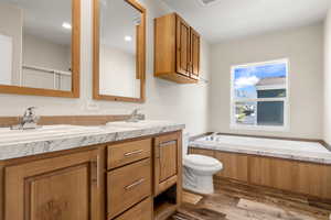 Full bathroom featuring a garden tub, double vanity, and dark wood-style flooring
