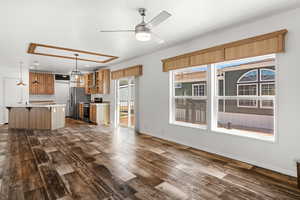 Kitchen with a breakfast bar area, appliances with stainless steel finishes, dark wood-type flooring, ceiling fan, and a center island with sink