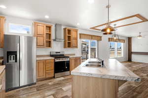 Kitchen with stainless steel appliances, wall chimney exhaust hood, light wood-style floors, a kitchen island with sink, and light countertops
